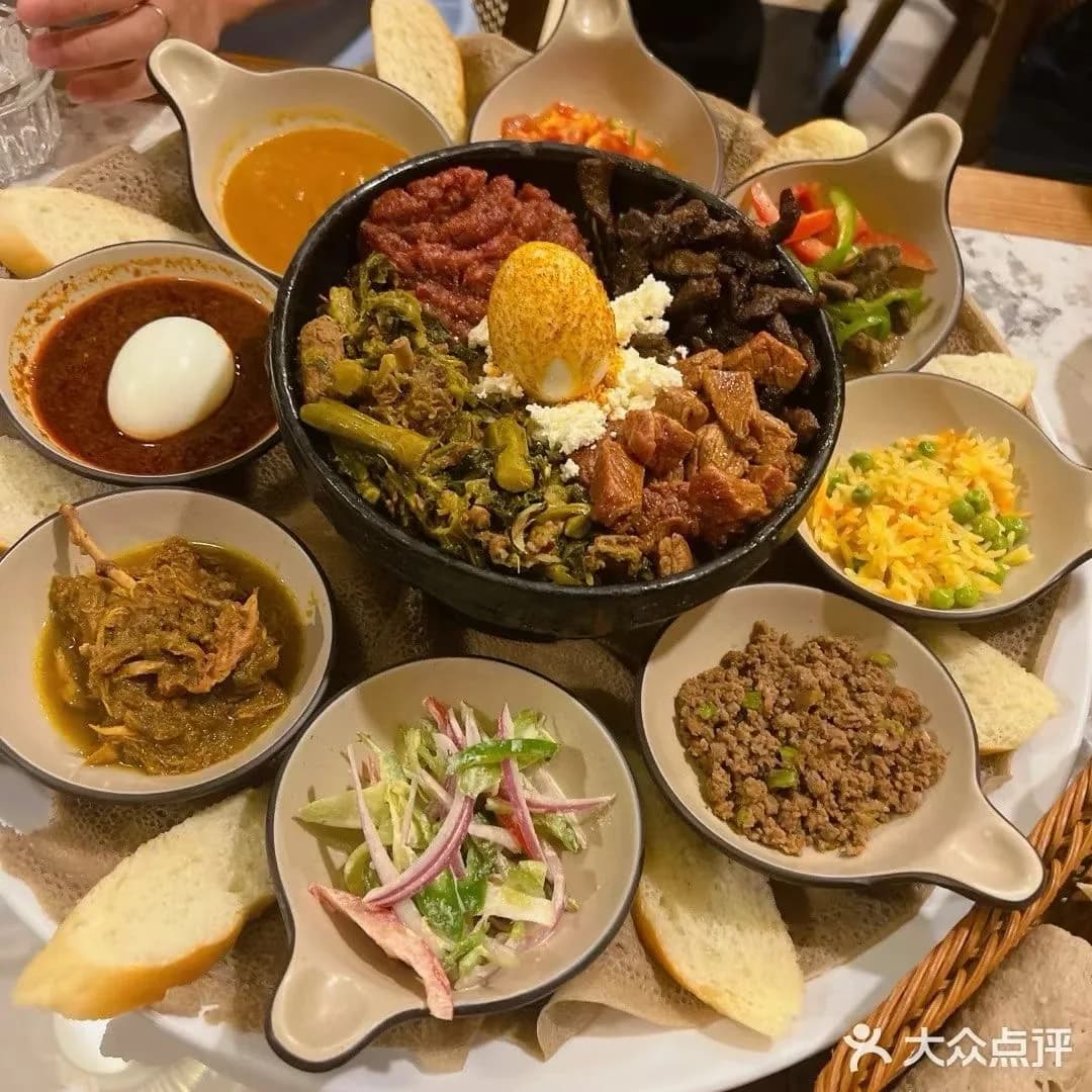 An overhead view of a mixed platter with an egg, greens, meat, stews, rice, salad, and bread.