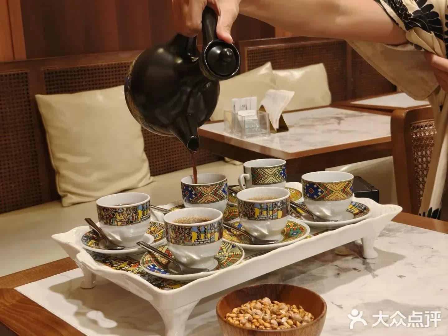 Coffee being poured from a black Ethiopian pot into colourful patterned cups on a serving tray.
