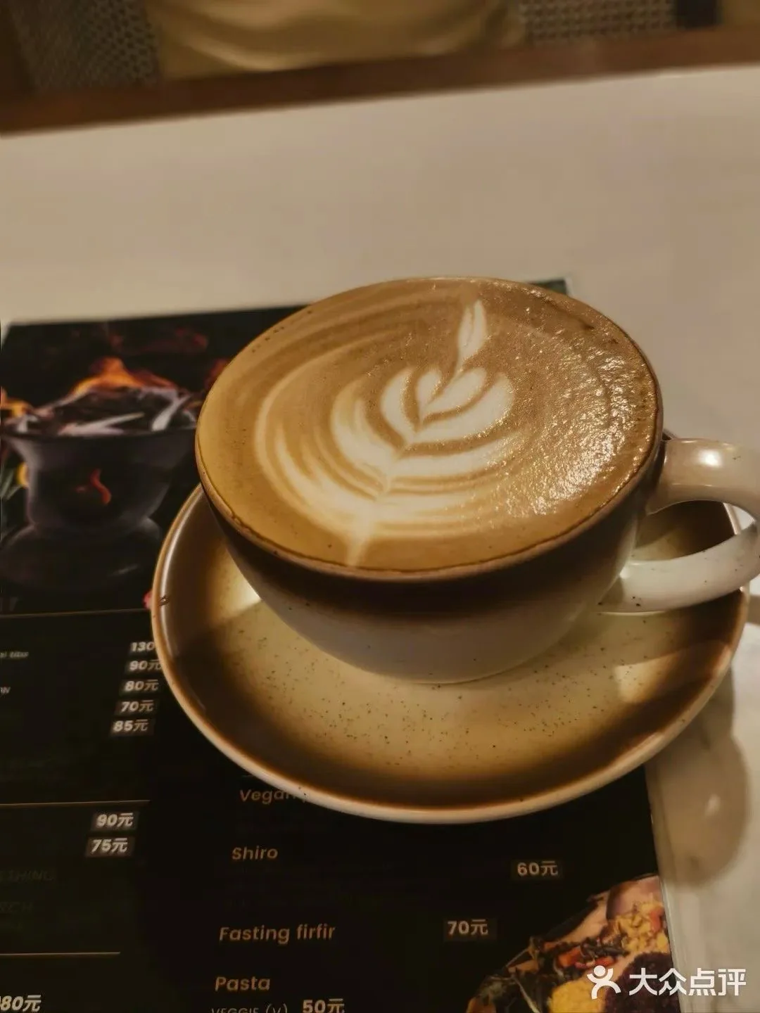 A latte with leaf-shaped foam art in a ceramic cup and saucer, resting over a dark menu.